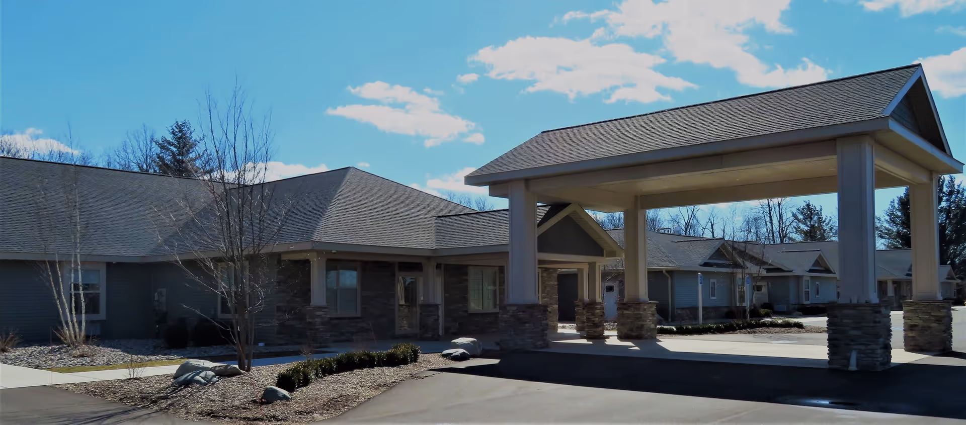 Front entrance of a single-story senior living facility with a covered porte-cochere and landscaped driveway.