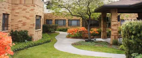 Brick senior residence exterior with curved walkway and manicured lawn.