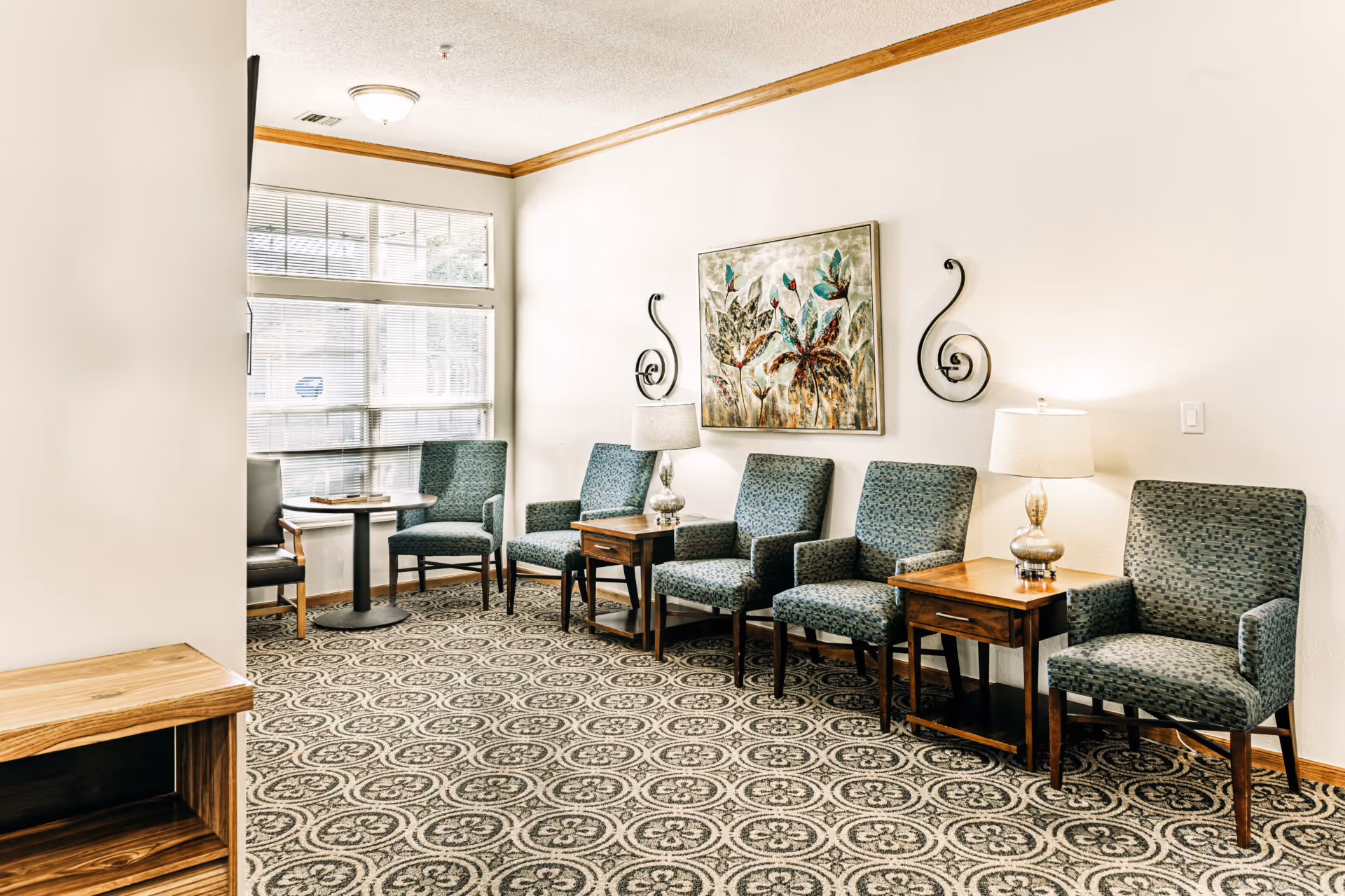 Bright communal seating area with upholstered chairs, side tables, lamps, and wall art.