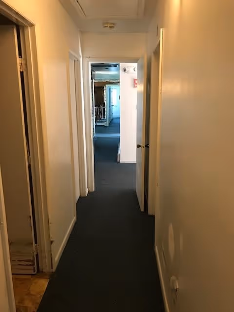 Narrow carpeted interior hallway with white walls and open doorways leading to rooms.