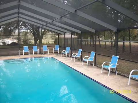 Outdoor pool area with blue lounge chairs under a covered patio.