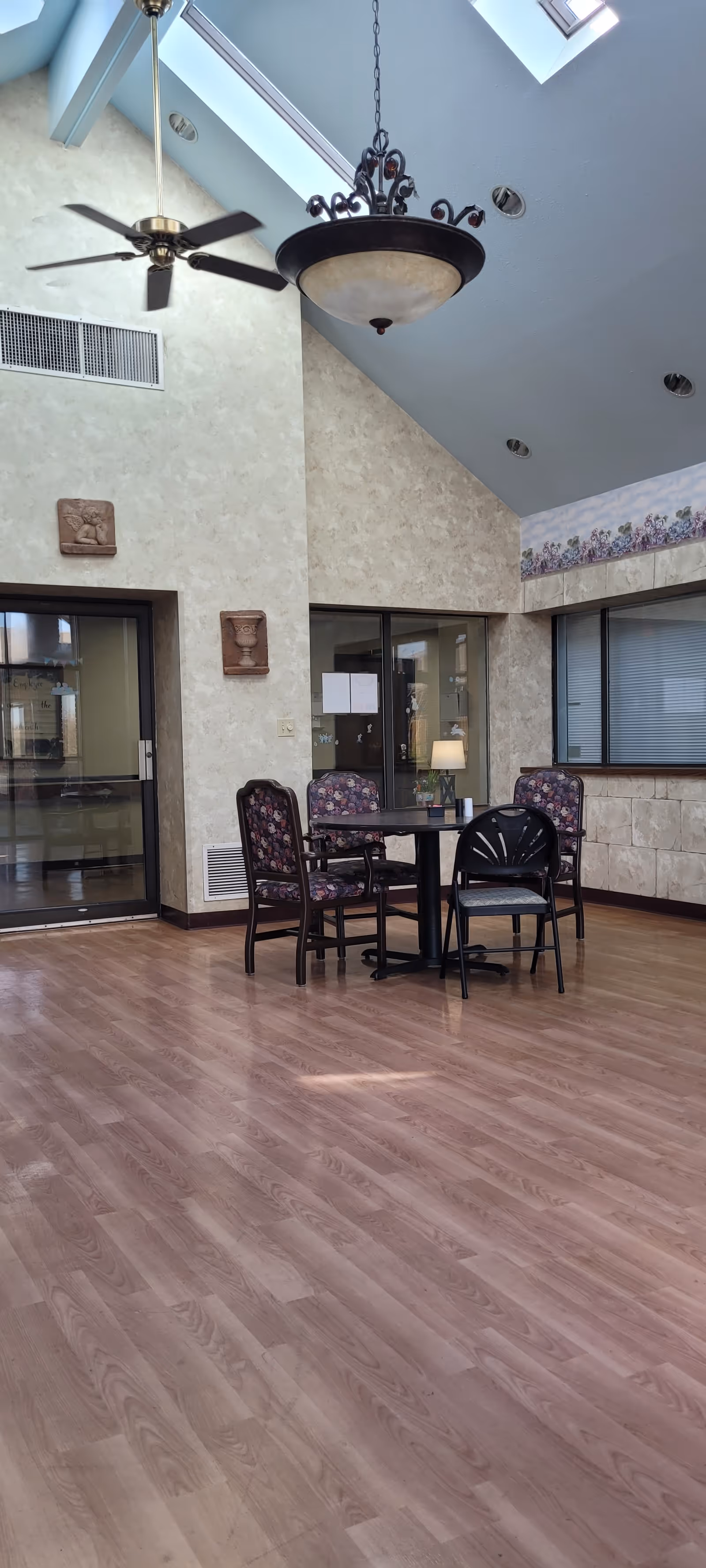 High-ceilinged interior lounge with a small round table and chairs beneath skylights and hanging light fixtures.