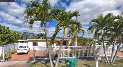 Exterior view of Premier Assisted Living with palm trees, a gated entrance, and parked cars.