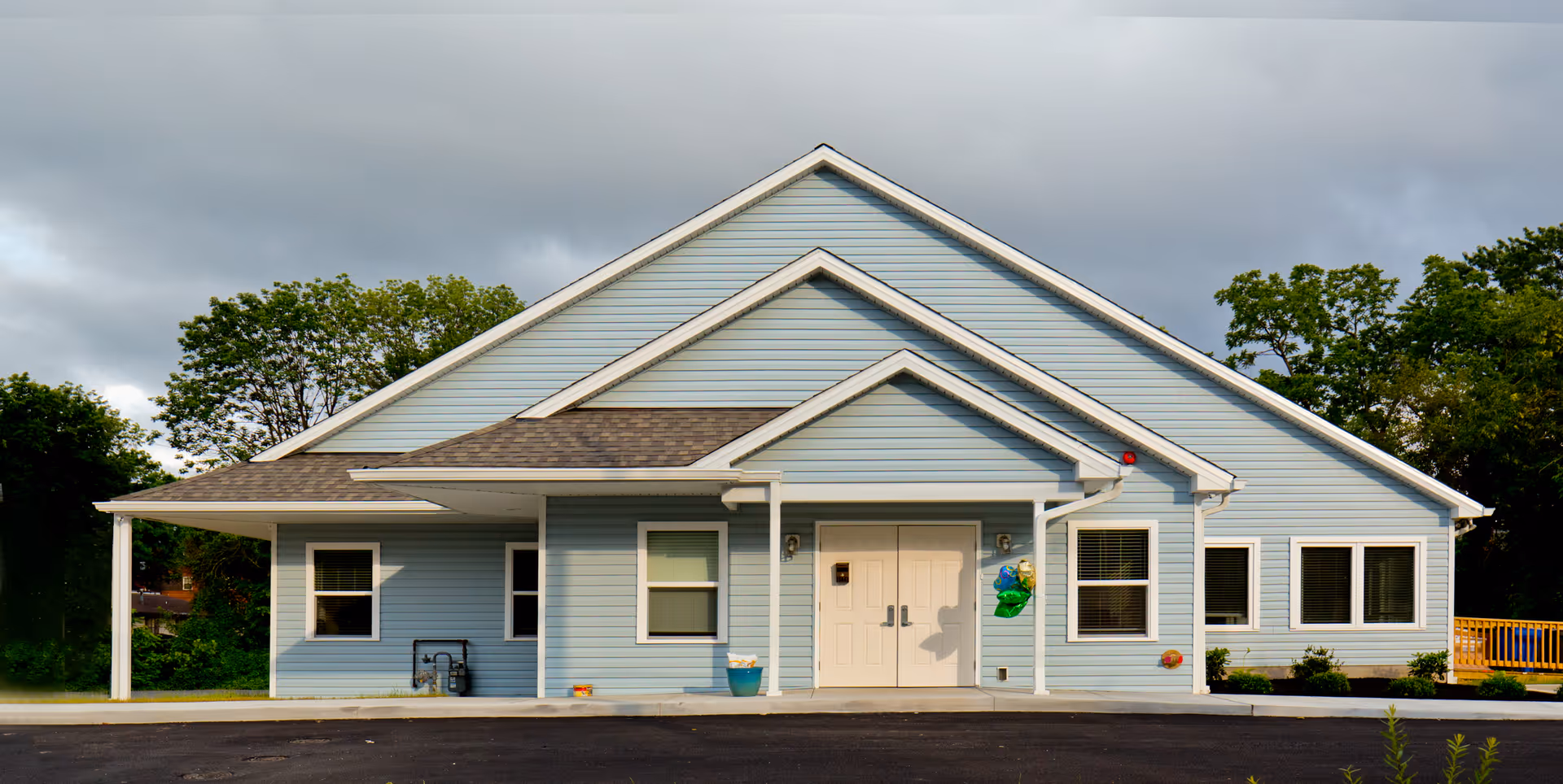Front exterior of a light-blue single-story building with a gabled roof and double entry doors.