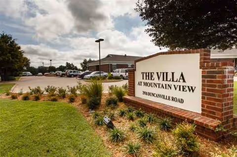 The Villa at Mountain View sign with brick pillars and a parking lot in front.