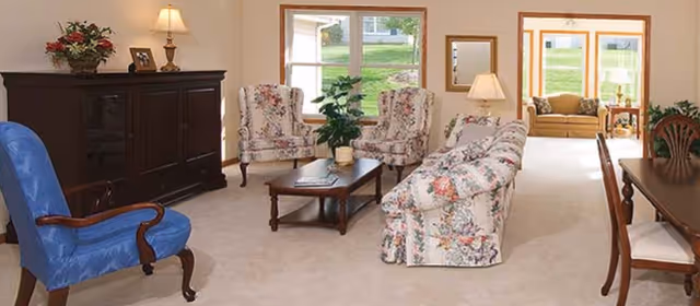 Bright living room with floral-upholstered sofa and chairs, a blue armchair, wooden coffee table and large windows.