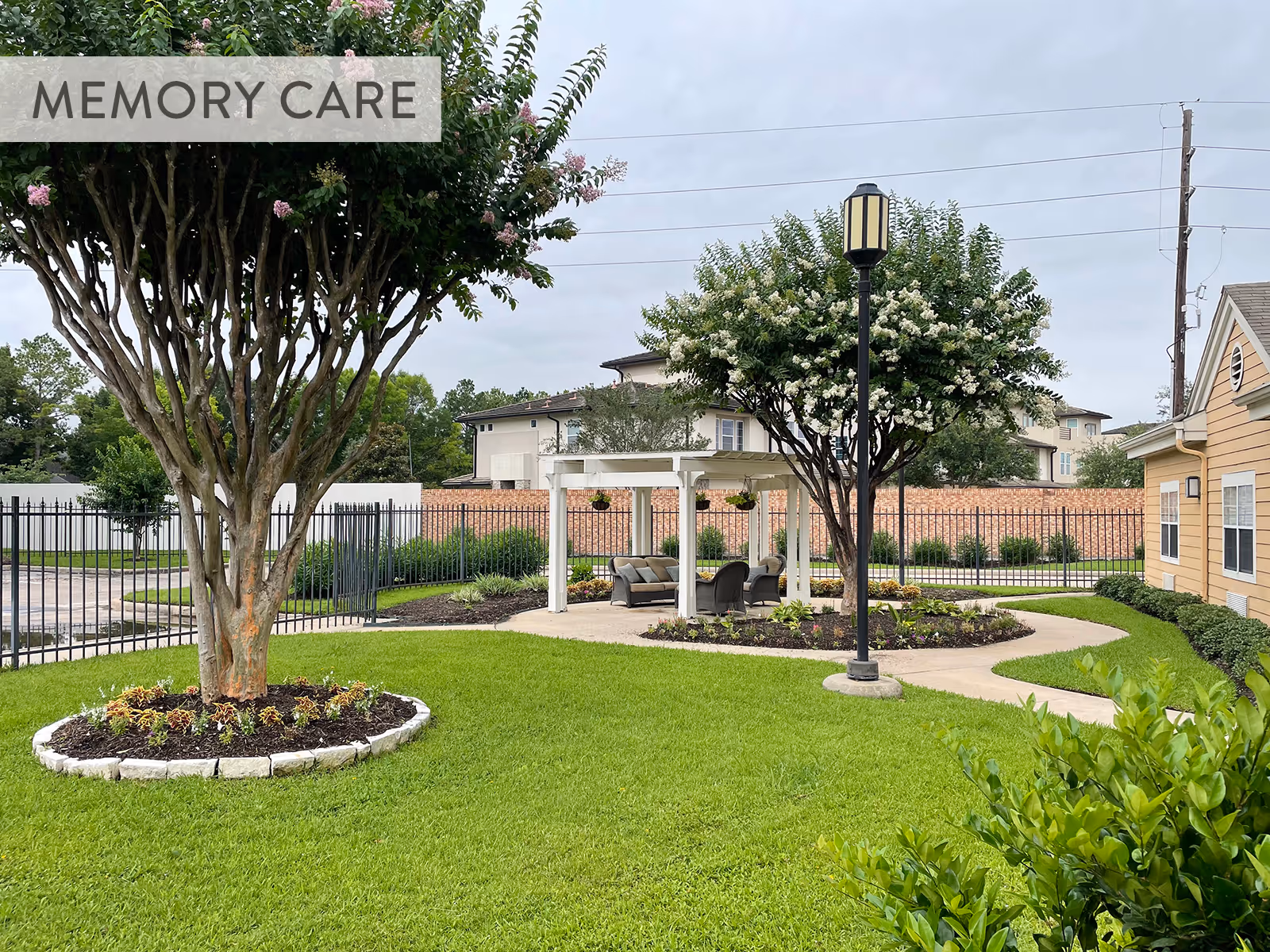 Landscaped outdoor courtyard with a pergola seating area, trees, a lamp post, and a manicured lawn.