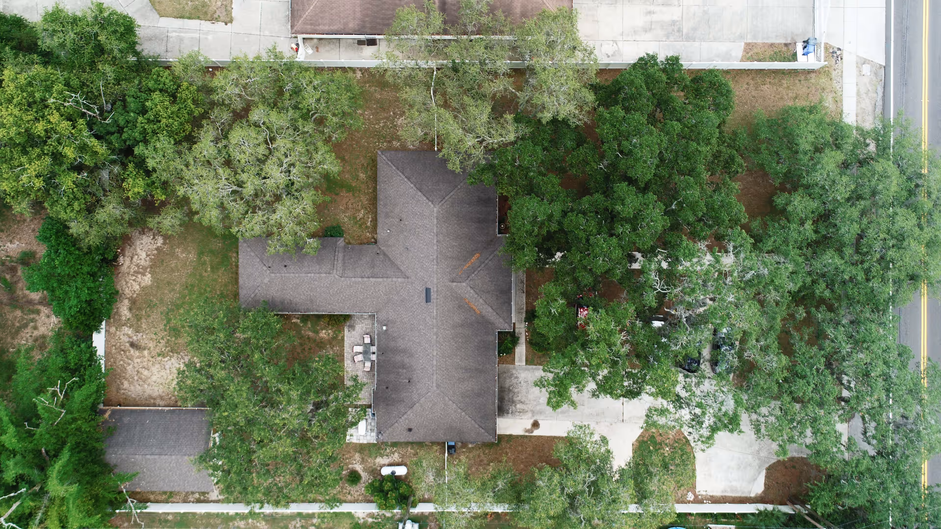 Aerial view of a residential building surrounded by trees and greenery, with a driveway and sidewalks visible around the property.