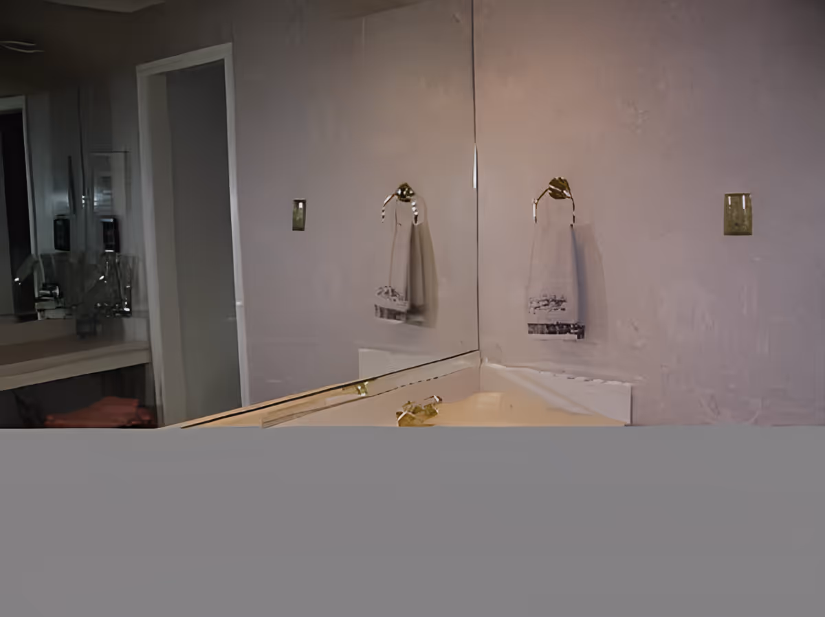 Corner bathroom vanity with a large mirror, countertop sink and a hand towel hanging on a ring.