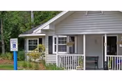 Light gray, house-style building with a porch, bench, and Coral Landing Assisted Living sign.