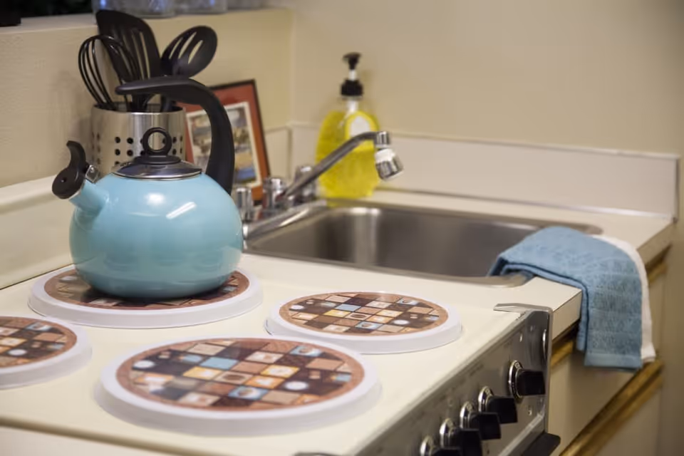 Small kitchen countertop with a blue kettle on the stove, sink, utensils and dish soap nearby.