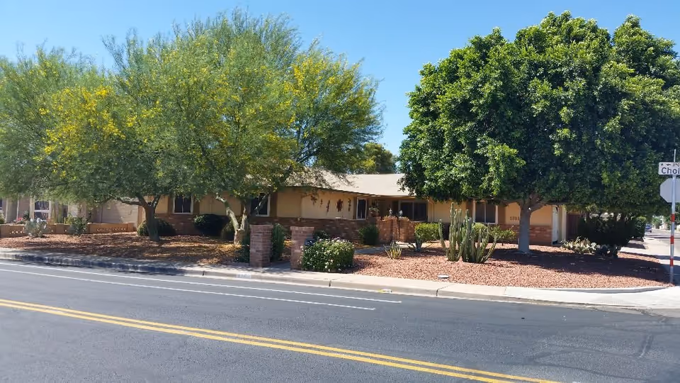 Front view of White Violet Adult Care Home II with trees and desert landscaping.