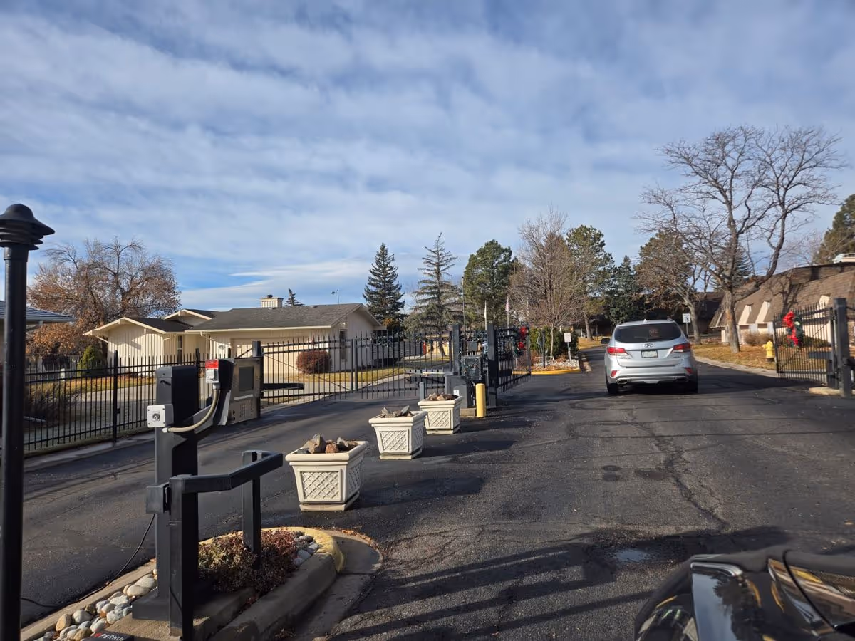Gated driveway entrance to a residential community with planter boxes, a security gate, and a car driving through.