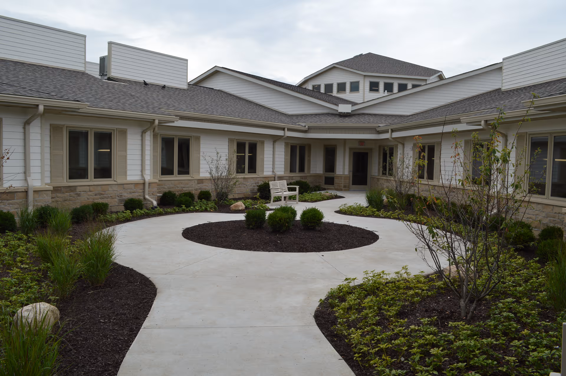 A landscaped central courtyard with a circular concrete walkway, planted beds, and a bench surrounded by single-story facility wings.