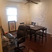 Small multipurpose room with a dark wood dining table and chairs, an office desk and chair, ceiling fan, and a window.