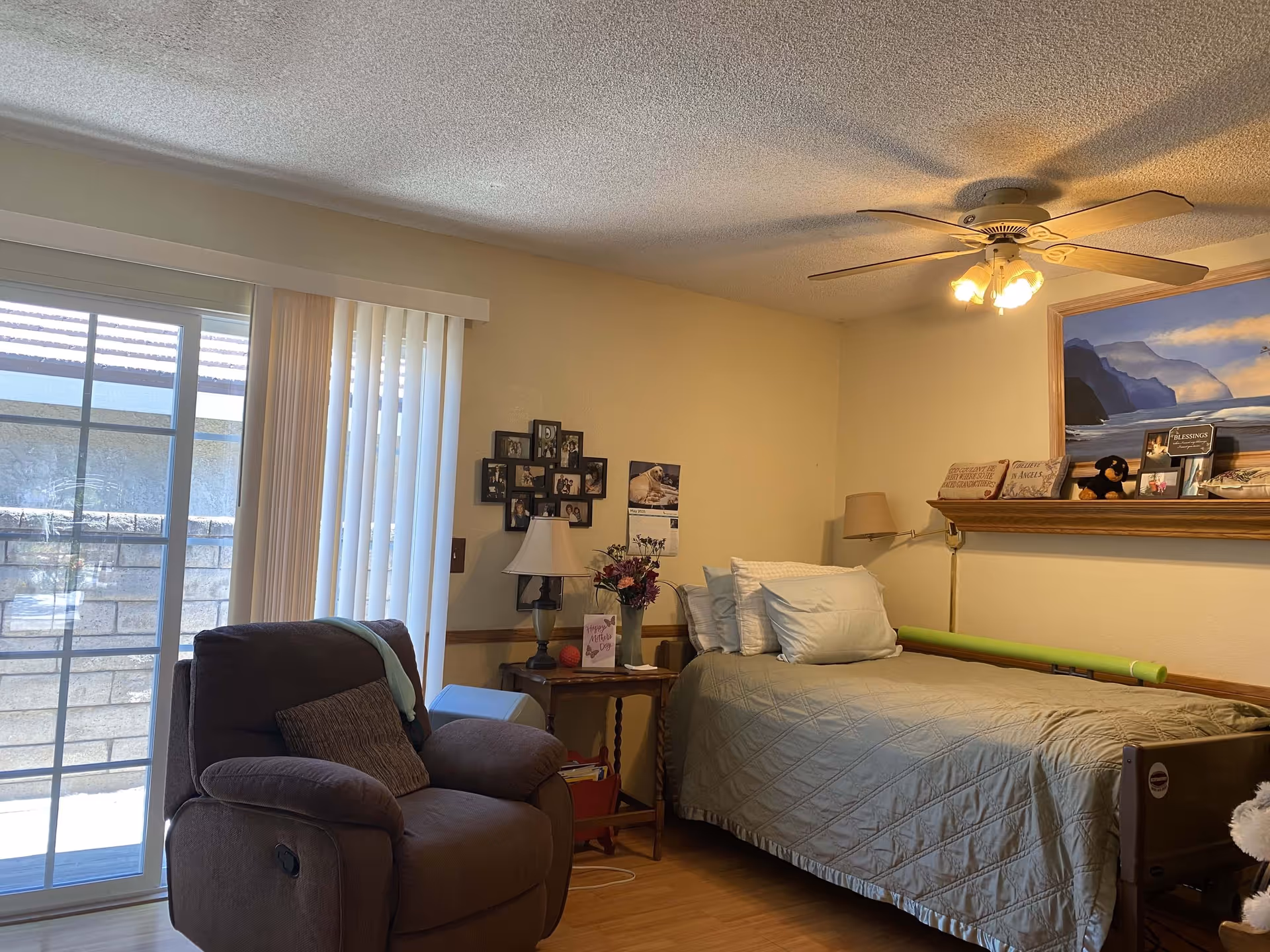 Cozy bedroom with a single bed, recliner chair, bedside table and sliding glass door to the outside.