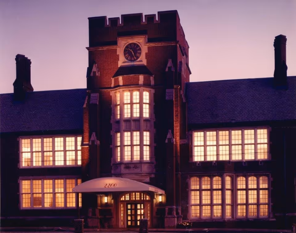 The Lorelton building at dusk with warm lights glowing from multiple large windows. The structure features a central tower with a clock and a canopy entrance displaying the number 2200.