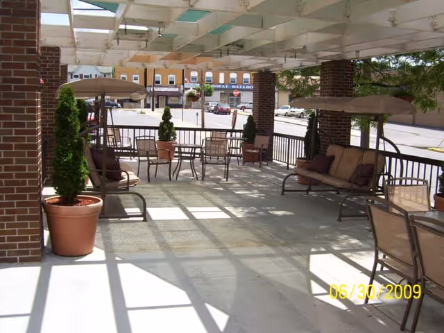 Covered outdoor patio with chairs, swings and potted plants overlooking a street and storefronts.