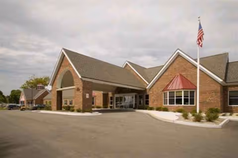 Brick senior living facility exterior with a covered entrance and American flag.
