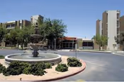 Front entrance of a senior living campus featuring a circular fountain in a driveway with multi-story buildings and trees under a clear sky.