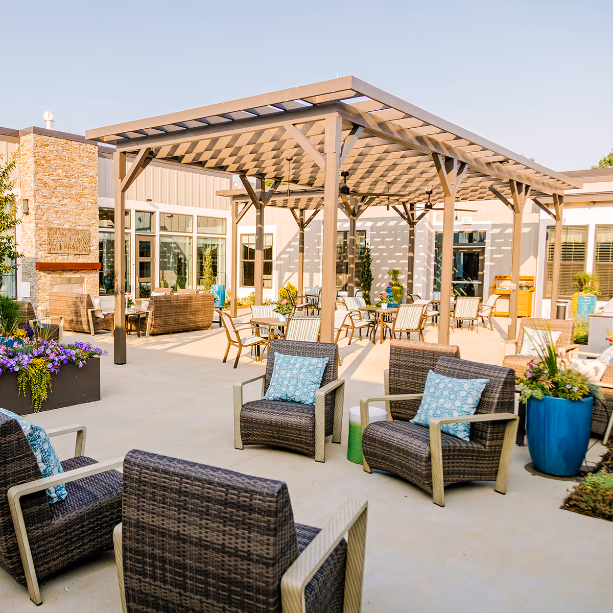 Outdoor courtyard with wicker chairs, tables, planters, and a large pergola at a senior living facility.