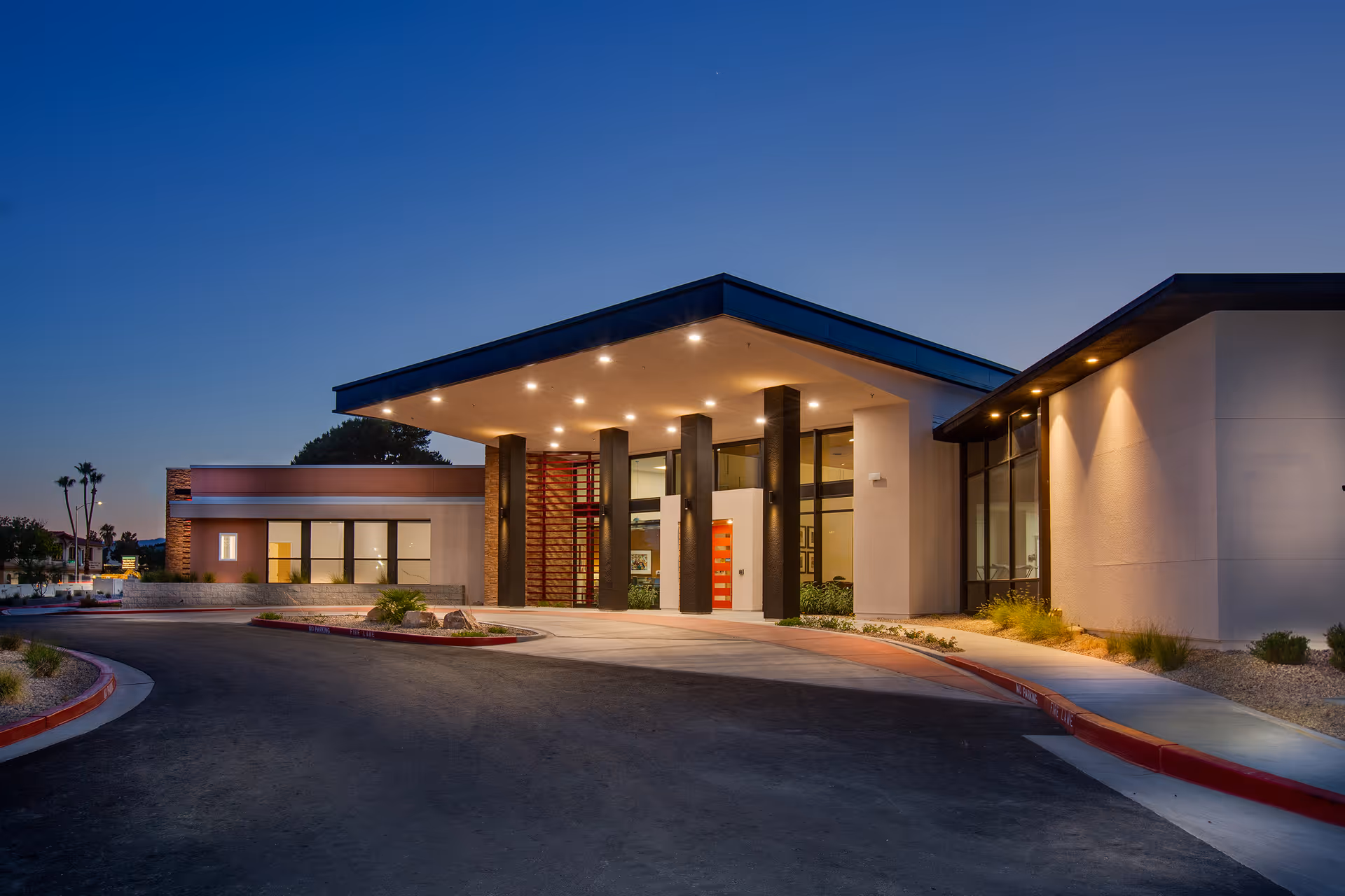 Dusk view of Lumina Las Vegas main entrance with a lit canopy, driveway drop-off, and landscaped grounds.