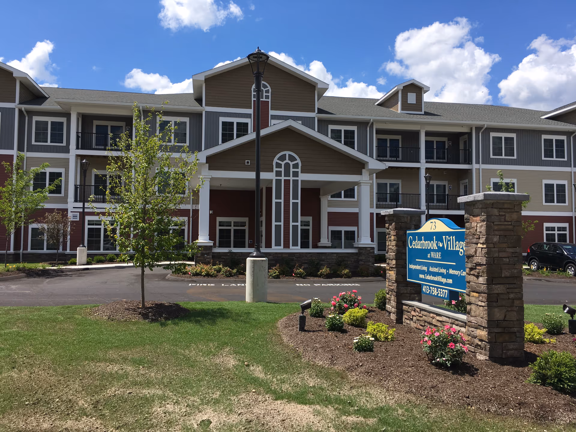 Front exterior of Cedarbrook Village senior living building with landscaped entrance and a sign.