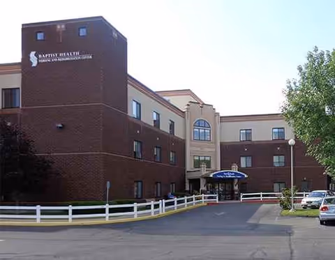 Exterior view of Baptist Health Nursing and Rehabilitation Center, brick building with entrance and parked cars.