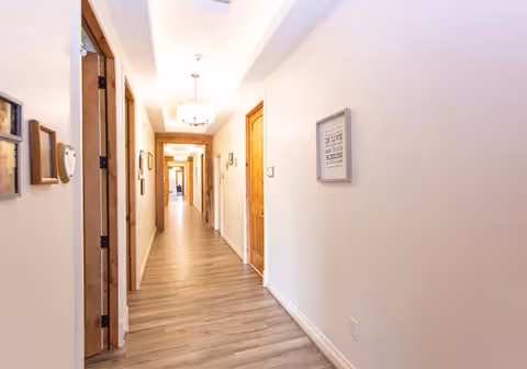 Well-lit interior hallway with wood doors, light-colored walls, framed artwork and wood-look flooring.