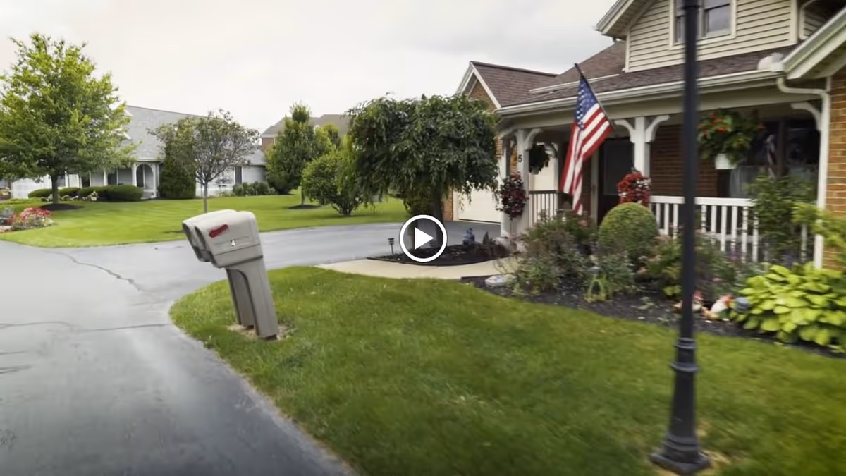 Front porches and landscaped lawns of several homes in a senior living community, with a mailbox and an American flag.