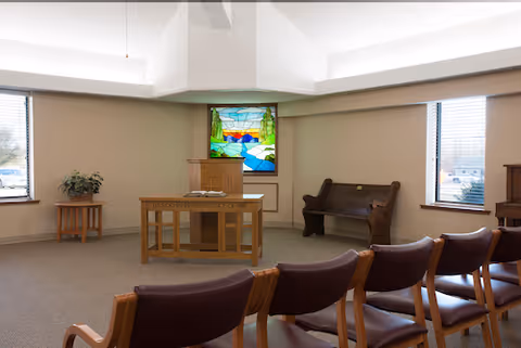 Small chapel-style common room with rows of chairs facing a wooden lectern and a stained-glass window.