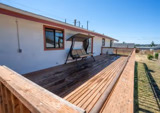 Wooden deck attached to a single-story building with a swing bench and railing, under a clear blue sky.