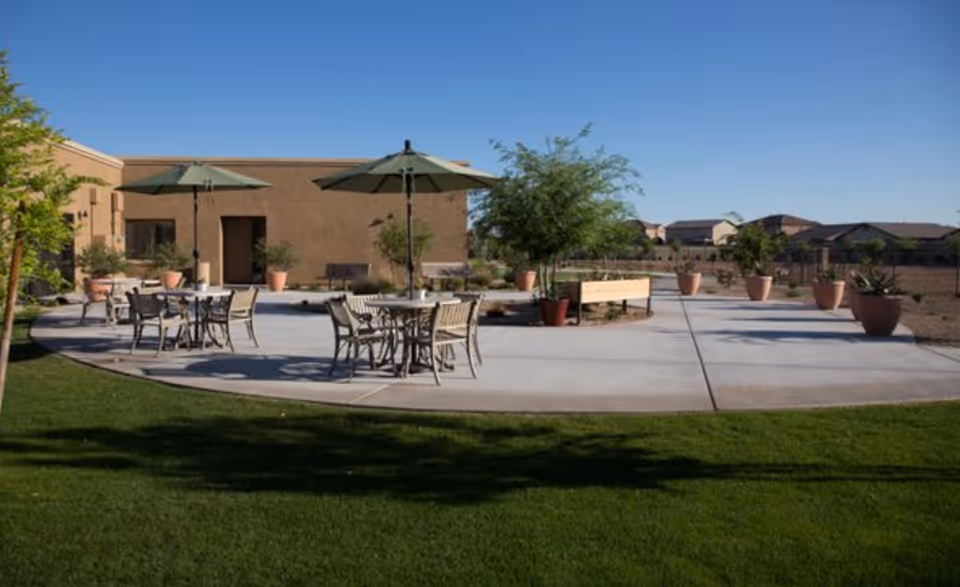 Outdoor patio with tables, chairs, umbrellas, and potted plants near a building.