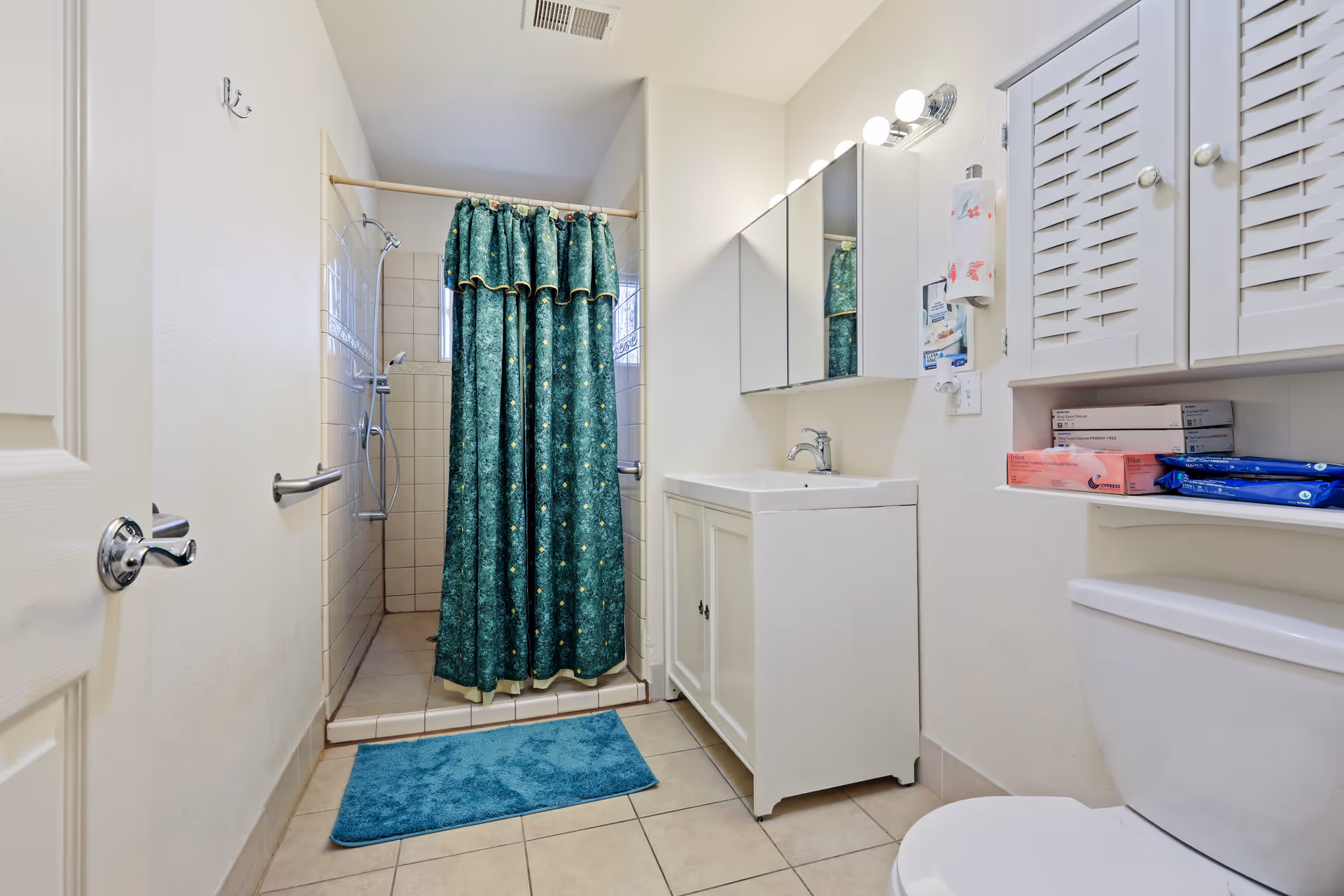Tiled bathroom featuring a walk-in shower with a green curtain, white vanity with mirror cabinet, and a toilet.