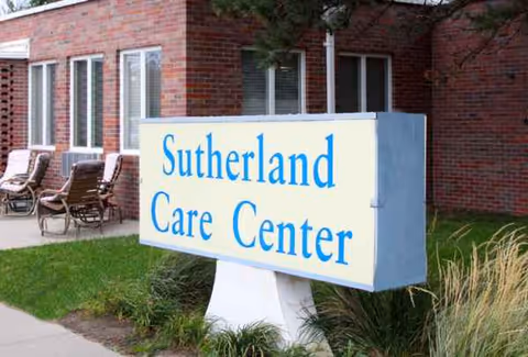 Brick building exterior with a sign reading Sutherland Care Center and outdoor chairs.