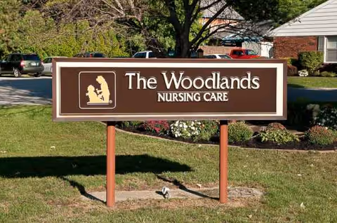 Outdoor sign reading The Woodlands Nursing Care on a grassy lawn in front