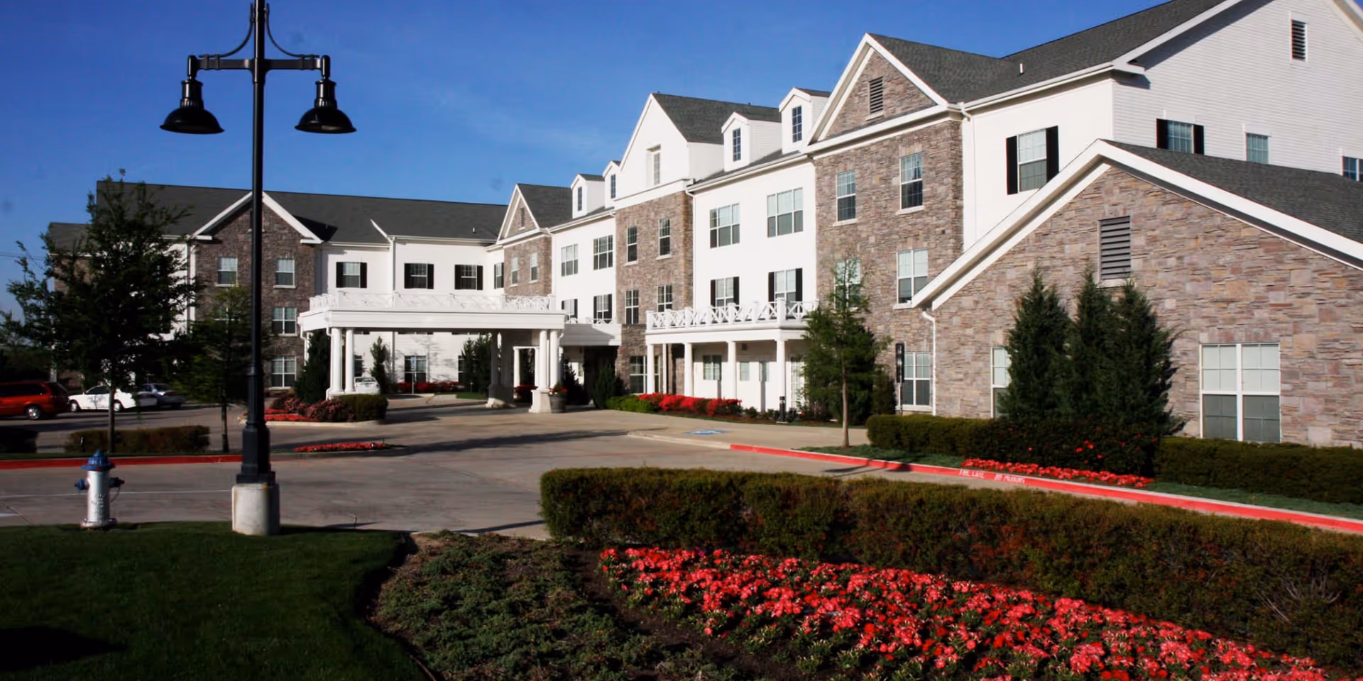 Exterior view of Prestonwood Court senior living facility with brick facade and landscaped entrance.