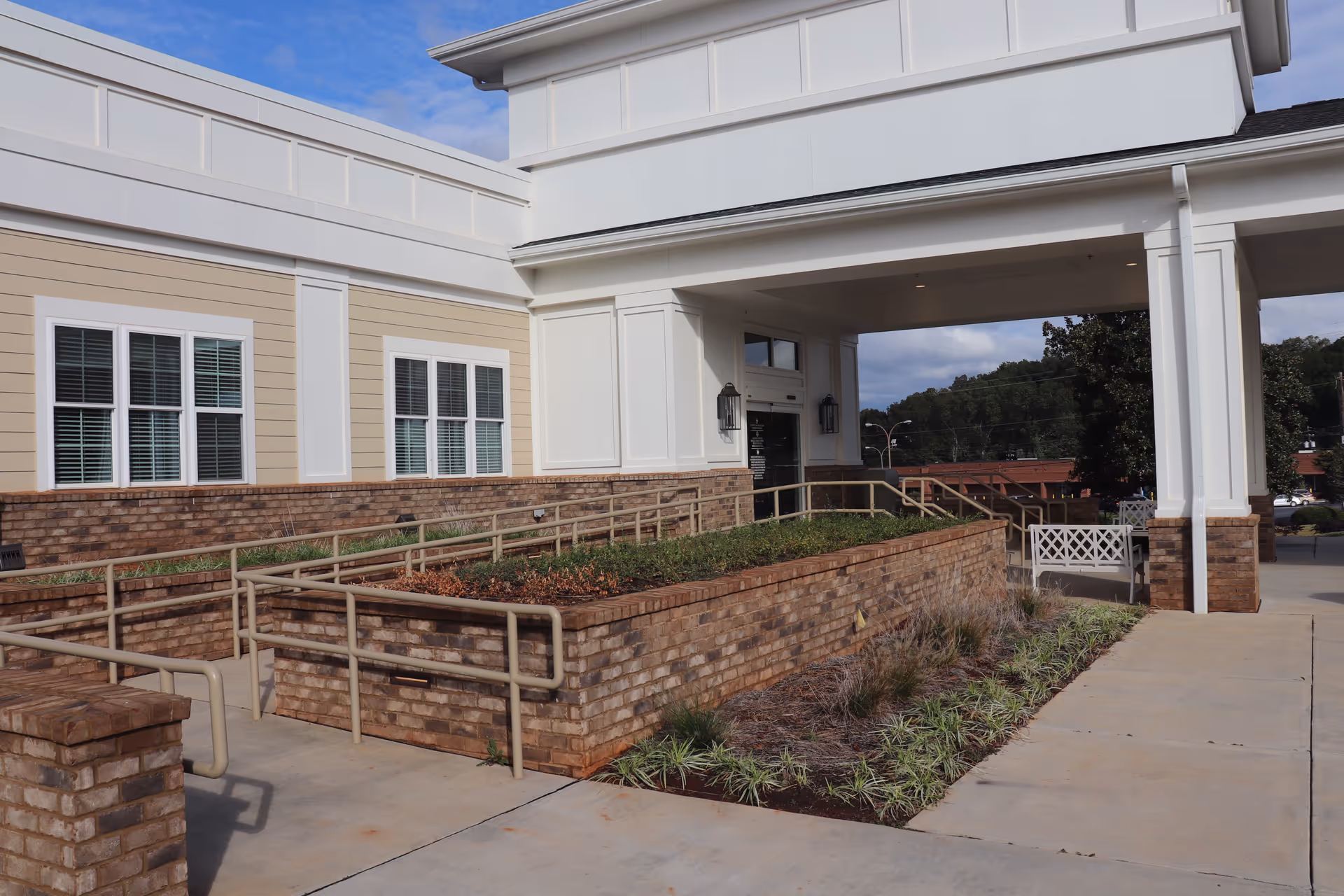 Covered building entrance with a white portico, brick planter beds, accessible ramps, and a paved walkway.