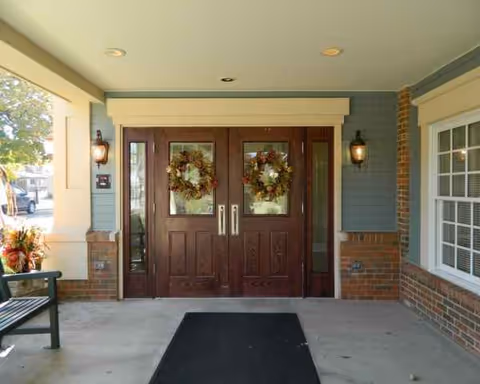 Double wooden doors with wreaths flank a brick-and-siding entrance under a covered porch.