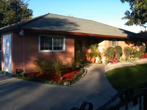 Front exterior view of Camelot Residential Homes, a single-story pink senior living house with landscaping.