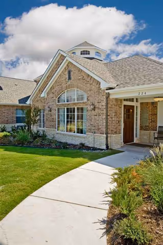 Brick senior living facility front with arched window, entryway, and manicured lawn.
