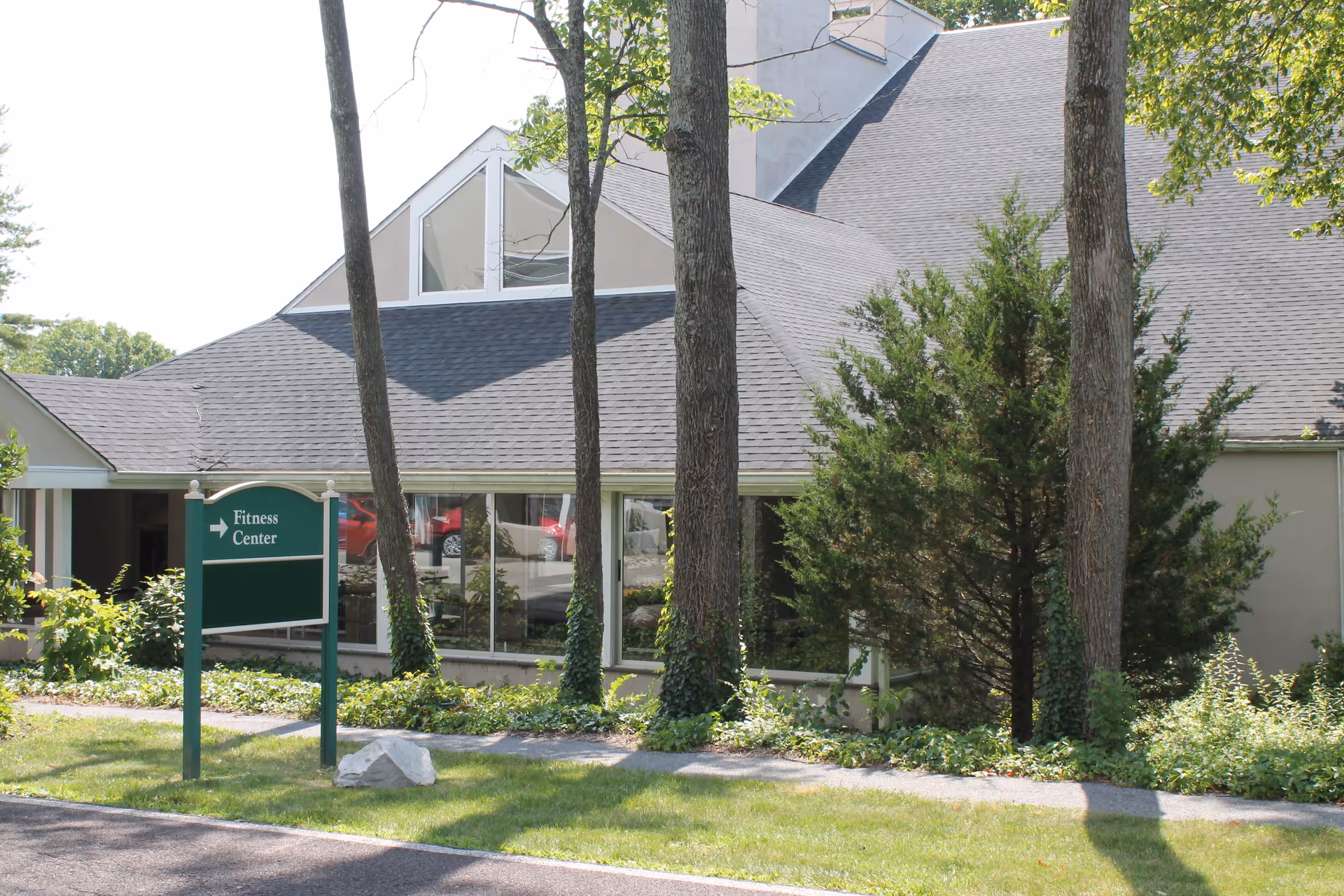 Exterior view of a building with large windows, trees, and a green 'Fitness Center' sign on the lawn.
