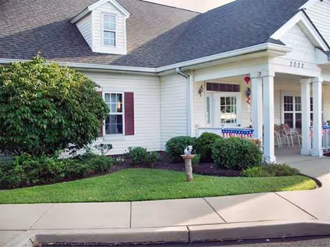 Front of a white senior living facility with a porch and green landscaping