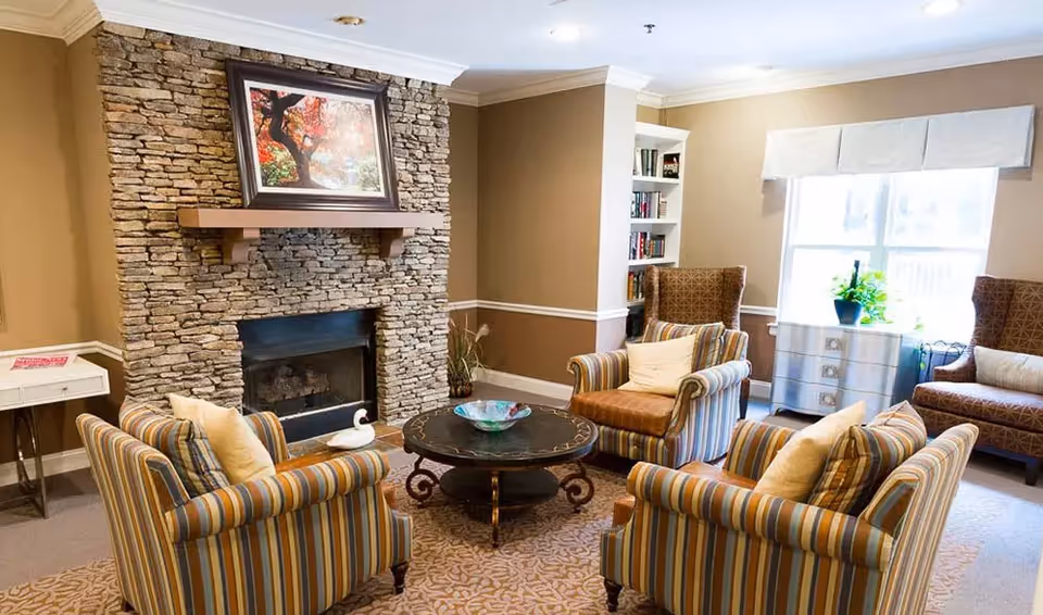 A cozy seating area with striped armchairs arranged around a round coffee table in front of a stone fireplace.