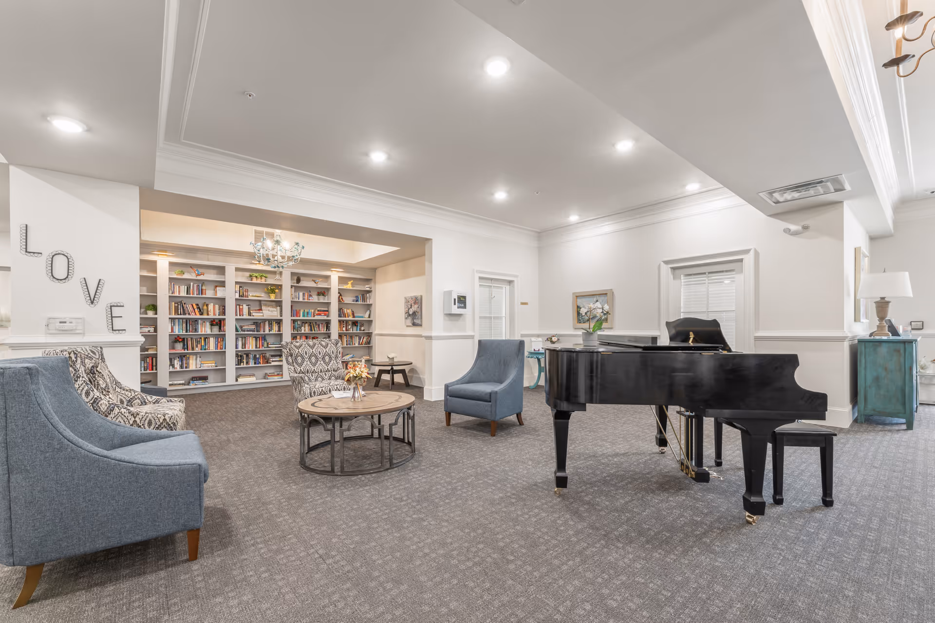 Bright communal lounge with a grand piano, seating area, and bookshelves.