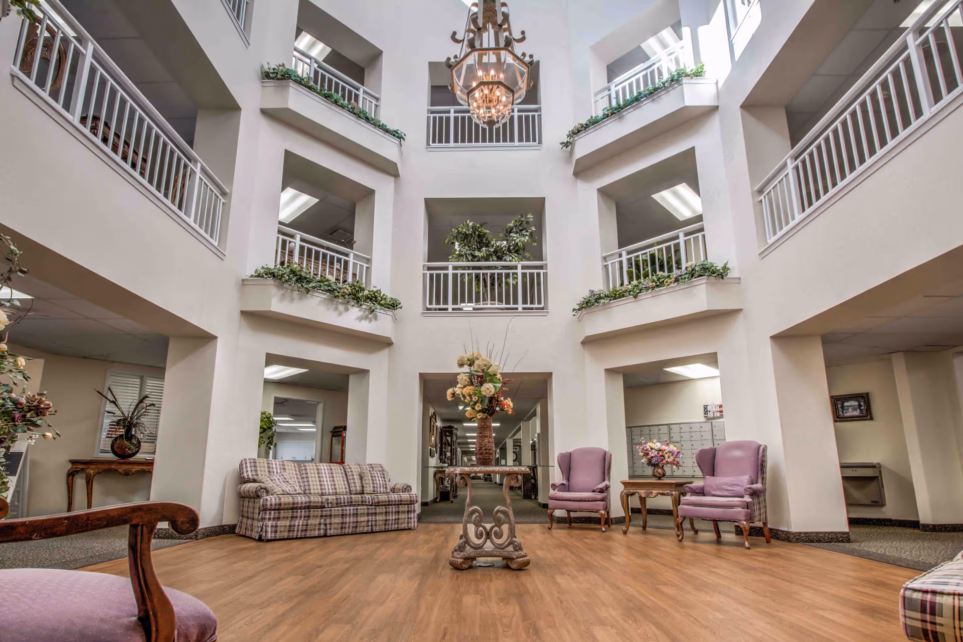 Spacious multi-story atrium lobby with seating, a central floral arrangement, balcony railings, and a chandelier.