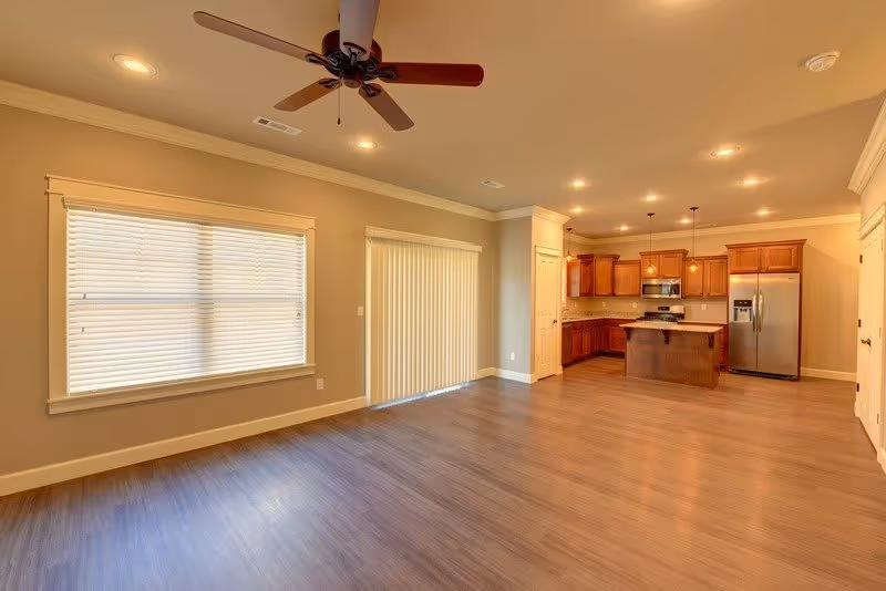 Open-plan living area with wood floors, a ceiling fan, large window and sliding glass door, and a kitchen with an island and stainless steel appliances.