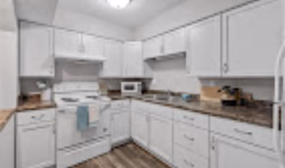 L-shaped kitchen with white cabinets, a stove, microwave and brown countertops.