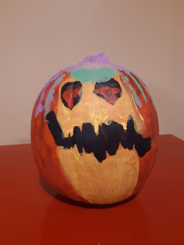 Hand-painted jack-o'-lantern pumpkin with colorful eyes and a black jagged mouth sitting on a red surface.
