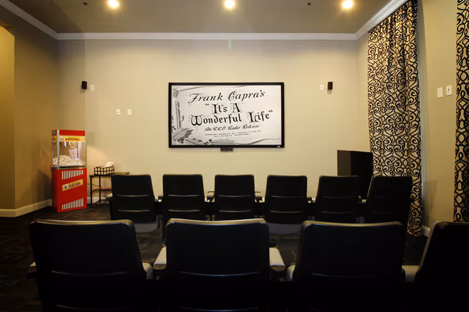 Small screening room with rows of theater chairs facing a screen showing 'It's A Wonderful Life' and a popcorn machine at left.